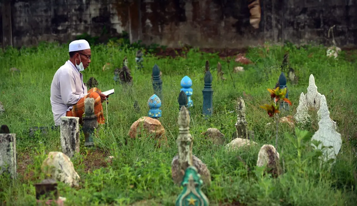 Seorang pria berdoa di sebelah makam kerabat saat perayaan Hari Raya Idul Adha di sebuah pemakaman di Provinsi Narathiwat, Thailand, Rabu (21/7/2021). Setiap Idul Adha atau hari besar Islam lainnya, sebagian warga banyak mendatangi kuburan untuk mendoakan keluarganya. (Madaree TOHLALA/AFP)