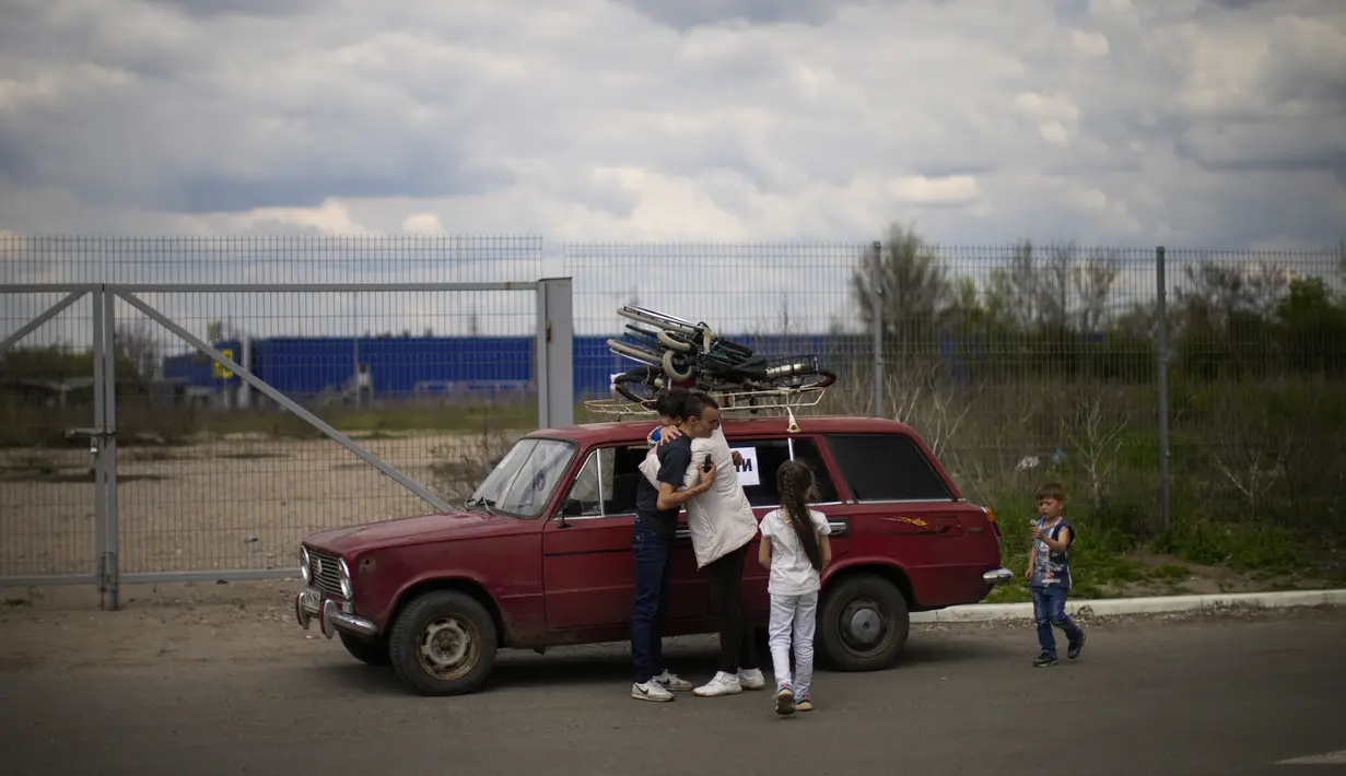 <p>Orlyanske (kiri) memeluk istrinya Kolya di samping mobil mereka saat mereka tiba dari Vasylivka ke pusat penerimaan pengungsi di Zaporizhzhia, Ukraina, Selasa (3/5/2022). Ribuan warga Ukraina terus meninggalkan wilayah yang diduduki Rusia. (AP Photo/Francisco Seco)</p>