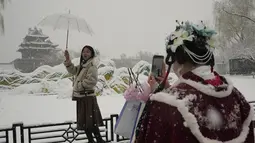 Seorang wanita berpose untuk foto di dekat Kota Terlarang saat salju turun di Beijing, China (18/3/2022). Sebagian besar distrik di ibu kota China, Beijing, mengalami salju pada hari Kamis, dengan distrik paling utara Yanqing melaporkan hujan salju terberat. (AP Photo/Ng Han Guan)
