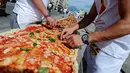 Koki ahli saat menyelesaikan pembuatan pizza terpanjang untuk mencetak rekor dunia, di sepanjang pinggir Laut Naples, Italia, 18 Mei 2016. Pizza itu memiliki ukuran sekitar 1 mil dan terbentang di sepanjang pinggir Laut Naples. (Mario LAPORTA/AFP)