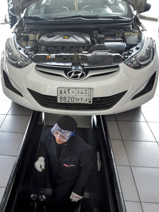Seorang mekanik wanita Saudi mengecek bagian bawah mobil di bengkel perbaikan dan servis di kota Jeddah, Arab Saudi (27/12/2021). Wanita Arab Saudi kini mulai mendapat kesempatan bekerja di area yang sebelumnya dianggap hanya identik pria seperti di toko suku cadang mobil di Jeddah. (AFP/Amer Hilabi