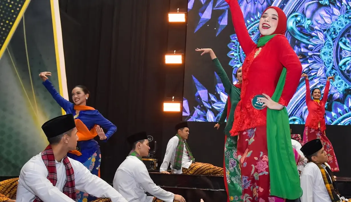 Saat performance, Isabel memilih kebaya encim berbordir merah yang dipadukan dengan kerudung serta bawahan batik bernuansa senada. Ia melengkapi busana ini dengan selendang hijau yang memberikan sentuhan dinamis sekaligus mempertegas garis siluet tradisional Betawi. Kombinasi warna merah dan hijau ini menjadi simbol semangat muda dan keberanian yang ia tunjukkan di atas panggung. [@isabel.azhari].