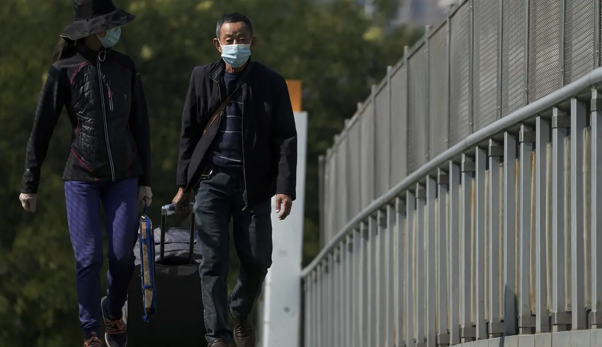 Pelancong mengenakan masker wajah dengan barang bawaan mereka berjalan di jembatan penyeberangan dekat stasiun kereta api di Beijing, Kamis (6/10/2022). Xinjiang yang luas adalah wilayah China terbaru yang terkena pembatasan perjalanan COVID-19, karena China semakin meningkatkan langkah-langkah pengendalian menjelang kongres penting Partai Komunis akhir bulan ini. (AP Photo/Andy Wong)