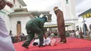 Petugas segera menolong Nur Elita, terpidana pelanggar hukum syariat, yang pingsan saat menjalani eksekusi hukuman cambuk di halaman Masjid Baiturrahim, Ulee Lheue, Banda Aceh, Senin (28/12).  (Jefta Images/dailymail.co.uk)