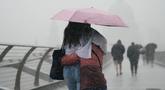 Orang-orang dengan payung berjalan di tengah hujan di Jembatan Milenium, London, Rabu (17/8/2022). Setelah berminggu-minggu cuaca terik, yang telah menyebabkan kekeringan dan membuat tanah kering, peringatan badai petir kuning dari Kantor Meteorologi memperkirakan hujan lebat dan badai petir yang bisa melanda bagian Inggris dan Wales. (Victoria Jones/PA via AP)