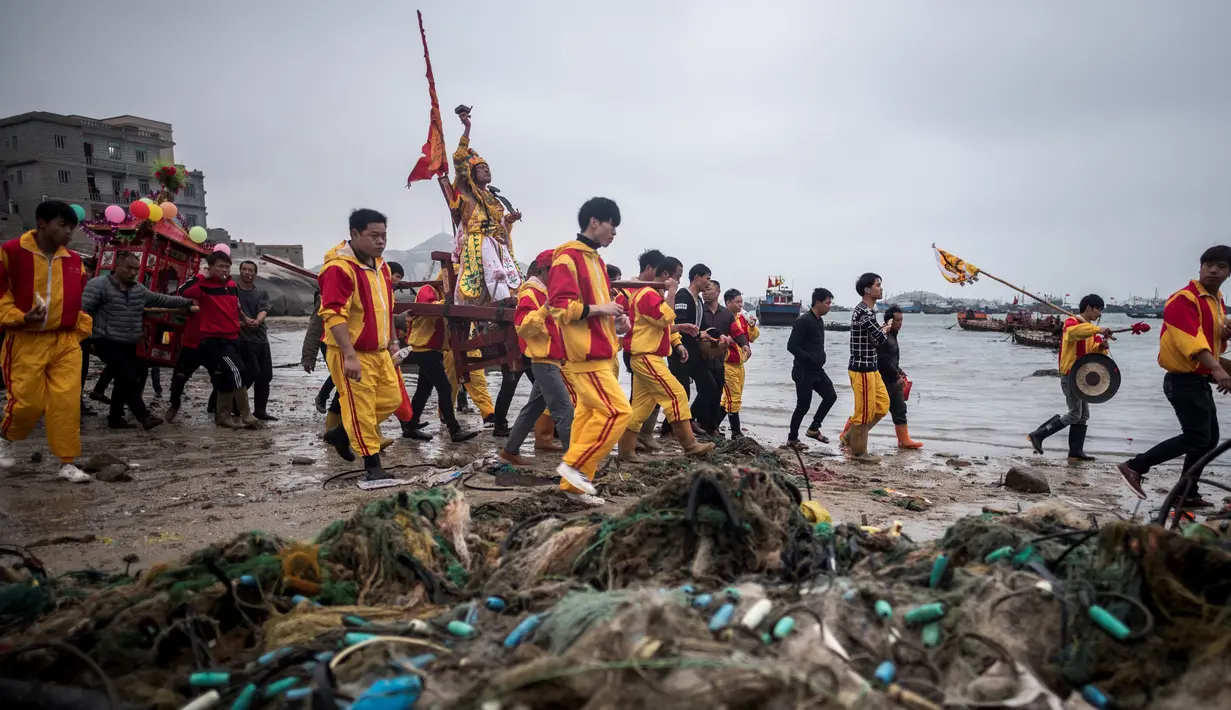 Penduduk desa menggunakan tandu membawa seorang pria berpakaian seperti Dewa Laut menuju pantai desa Fuye, Provinsi Fujian, Tiongkok (5/3). Ritual ini untuk meminta tangkapan ikan yang melimpah. (AFP Photo/Johannes Eisele)