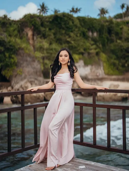 Gaun pink pudar tanpa lengan ini memanjang hingga menutupi kaki Lyodra Ginting. Keanggunannya menguat berkat rambut hitam yang dibiarkan tergerai plus anting. Ia bersandar di pagar berlatar bukit karang berhias pepohonan yang membaur dengan bibir laut. “Ngerti kan kenapa butuh sandaran,” tulis Lyodra Ginting bersama foto yang diunggah pada 8 Juli 2022. (Foto: Dok. Instagram @lyodraofficial)