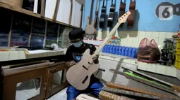 Pekerja menyelesaikan pembuatan gitar listrik Syukey Instrumen di kawasan Ciputat Timur, Tangerang Selatan, Banten, Selasa (26/10/2021). Dalam sebulan, pekerja mampu memproduksi 3 - 4 gitar listrik dengan harga Rp 3,5 juta hingga Rp 45 juta. (merdeka.com/Arie Basuki)
