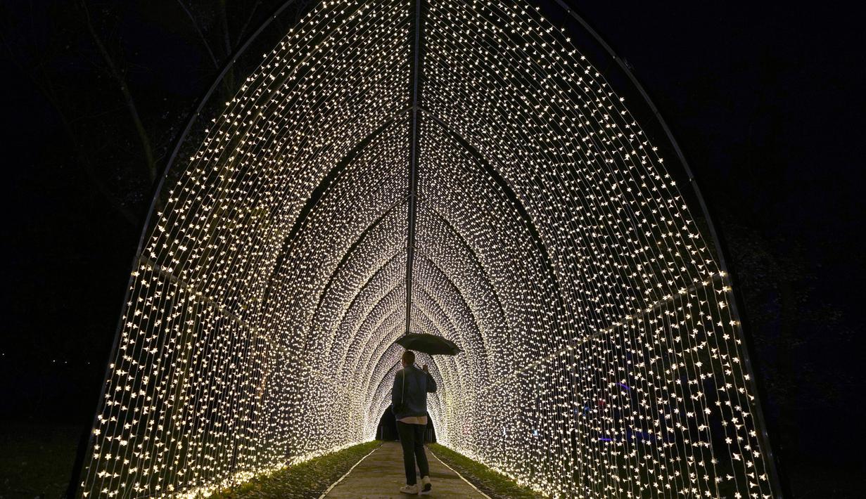 Seorang pria berjalan melalui terowongan lampu, bagian dari instalasi cahaya yang dipamerkan menyambut Natal di Royal Botanic Gardens, Kew, London, Selasa (15/11/2022). Selain memamerkan jalur cahaya dengan satu juta lampu di jalur sepanjang 2,7 km, terdapat cahaya imersif, pohon lampu, terowongan cahaya, dan pertunjukkan cahaya air yang mengesankan. (AP Photo/Kirsty Wigglesworth)