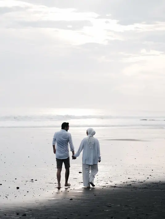 Nikmati keindahan pantai sembari jalani pemotretan pasangan ini makin terlihat romantis. Berpegangan tangan sambil tatapan mesra, jepretan foto ini mempelihatkan kehangatan hubungan Aryani Fitriana dan Donny Michael. Suasana pantai dengan deburan ombak membuat suasana sekitar makin syahdu. (Liputan6.com/IG/@aryanifitriana24)