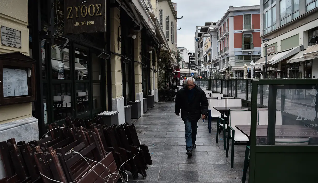 Seorang pria berjalan melewati kafe dan restoran yang tutup di Thessaloniki, Yunani, Selasa (16/11/2021). Pemilik restoran, kafe, dan bar melakukan pemogokan selama 24 jam, memprotes aturan terkait Covid-19 dan biaya energi yang tinggi. (Sakis MITROLIDIS / AFP)