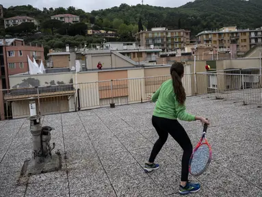 Vittoria Oliveri (depan) bermain tenis dengan Carola di atas atap rumah mereka selama lockdown COVID-19 di Finale Ligure, Wilayah Liguria, Italia (19/4/2020). Setiap hari Carola, 11, dan Vittoria, 13, bermain tenis dari satu atap ke atap lain di rumah mereka untuk berlatih. (AFP/Marco Bertorello)