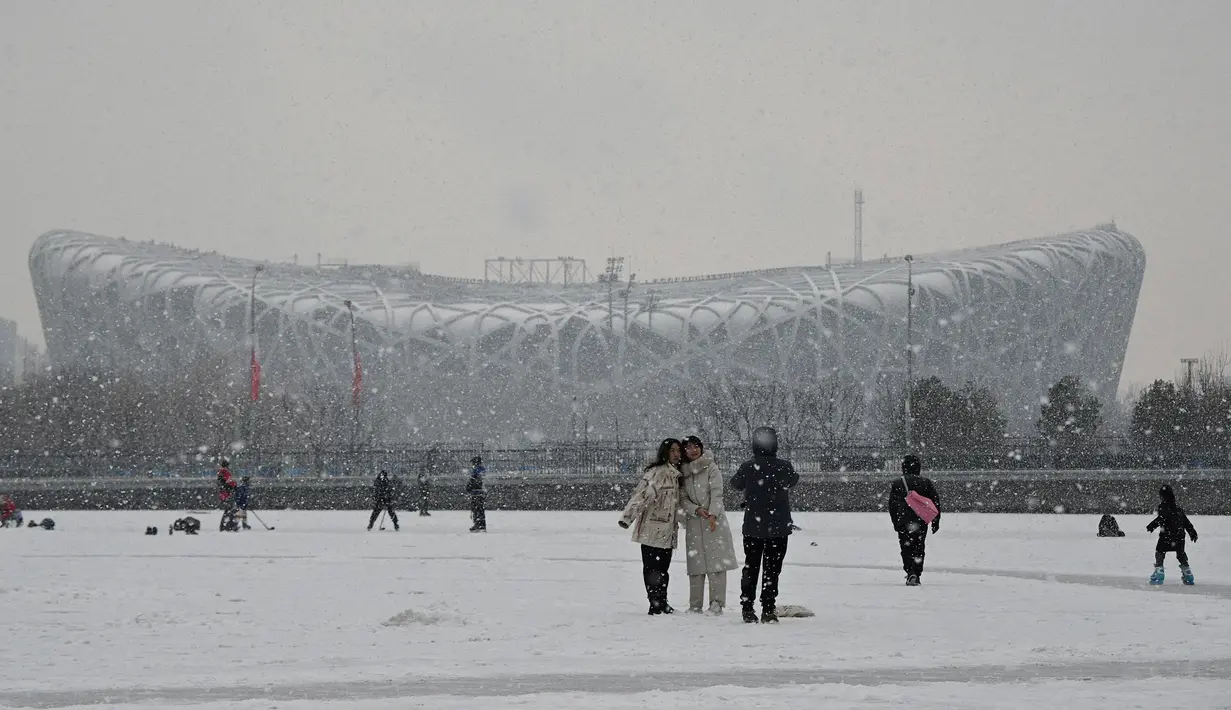 Orang-orang berpose untuk berfoto di kanal beku dan Bird's Next Stadium di Taman Olimpiade, dua minggu sebelum dimulainya Olimpiade Musim Dingin Beijing 2022, pada hari bersalju di Beijing pada 20 Januari 2022. (Noel Celis / AFP)