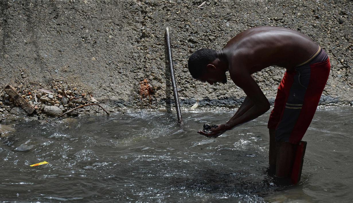 Seorang pria mengeluarkan lumpur dari dasar saluran pembuangan saat dia mencari logam berharga di Sungai Guaire, di Caracas, Venezuela (1/2). Puluhan warga mencari logam atau tembaga setiap hari di Sungai Guaire. (AFP Photo/Federico Parra)