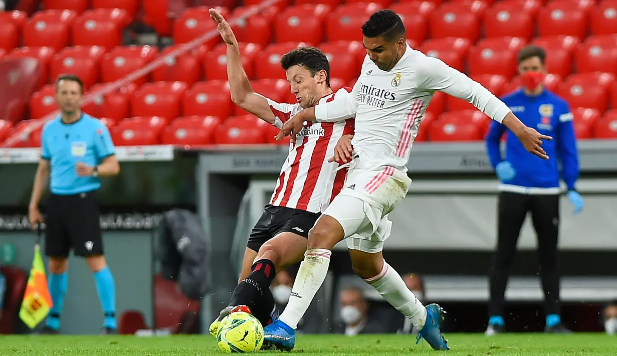 Gelandang Athletic Bilbao, Mikel Vesga (kiri) bersaing dengan gelandang Real Madrid, Casemiro pada pekan ke-37 La Liga di San Mames, Minggu (15/5/2021). Real Madrid berhasil menang di laga sulit yang berlangsung di markas Bilbao dengan skor tipis 1-0. (Ander GILLENEA / AFP)