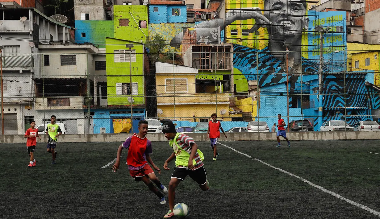 Aksi anak-anak saat bermain sepak bola di sebuah lapangan di Jardim Peri, Sao Paulo, Brasil, Minggu (20/5). Sebuah mural raksasa bergambar pemain sepak bola profesional Gabriel Jesus menghiasi permukiman mereka. (AP Photo/Andre Penner)