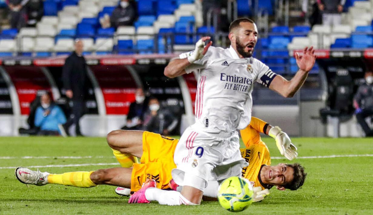 Striker Real Madrid, Karim Benzema, terjatuh saat berebut bola dengan kiper Sevilla, Bruno, pada laga Liga Spanyol di Stadion Alfredo di Stefano, Minggu (10/5/2021). Kedua tim bermain imbang 2-2. (AP/Manu Fernandez)