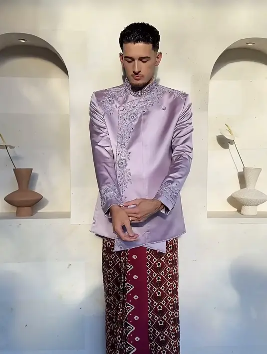 Melengkapi tampilannya dengan bawahan kain batik warna merah kecoklatan. Serta sandal slop warna ungu senada. [@kunsoomakeupartist]