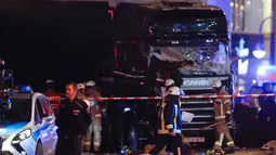 Petugas pemadam berjalan di depan truk yang menabrak kerumunan orang di sebuah pasar Natal di pusat Kota Berlin, Jerman, Senin (19/12). Kepolisian belum dapat memastikan identitas sopir truk berpelat nomor Polandia tersebut. (REUTERS/Fabrizio Bensch)