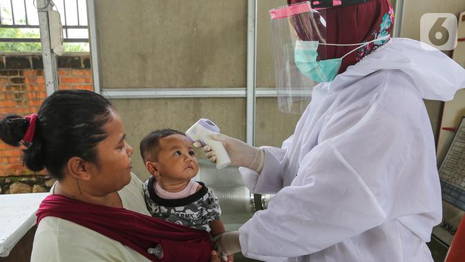 Bidan lengkap dengan baju Alat Pelindung Diri (APD) mengukur suhu tubuh pada anak di Posko Imunisasi, Kelurahan Bakti Jaya, Tangerang Selatan, Senin (11/5/2020). Pelayanan imunisasi tetap berjalan sesuai jadwal meski pandemi Covid-19. (Liputan6.com/Fery Pradolo)
