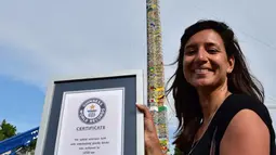 Seorang wanita berpose dengan sertifikat dari Guinness World Record, Itali, Minggu (21/6/2015).  Di belakang wanita tersebut tampak menara lego setinggi 35.50 meter. (AFP Photo/Giuseppe Cacace) 