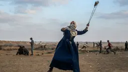 Wanita Palestina memakai ketapel untuk melemparkan batu ke arah pasukan Israel saat bentrok di Khan Yunis, Jalur Gaza, Jumat (13/9/2019). Unjuk rasa ini digelar setiap Jumat untuk menuntut kepulangan ke Tanah Palestina. (SAID KHATIB/AFP)