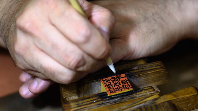 Gambar pada 9 Oktober 2020 menunjukkan pembuat stempel tinta tradisional Takahiro Makino, 44, menulis karakter pada hanko di sebuah studio di Tokyo. Perdana Menteri Yoshihide Suga tengah menggencarkan upaya digitalisasi dan menghapus Hanko atau stempel tinta tradisional Jepang. (Philip FONG/AFP)