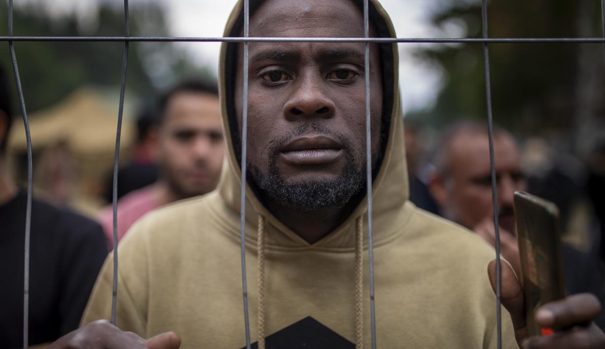 Seorang migran berdiri di pagar di kamp pengungsi di tempat latihan militer Rudninkai, Lithuania, Rabu (4/8/2021). Palang Merah memperingatkan keputusan Lituania untuk menolak imigran yang berusaha untuk menyeberang dari Belarusia tidak sesuai dengan hukum internasional. (AP Photo/Mindaugas Kulbis)