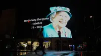 Seorang pria berjalan dengan payung melewati gambar Ratu Elizabeth II yang diproyeksikan ke layar besar di Piccadilly Circus, di London, Kamis, 8 September 2022. Ratu Elizabeth II meninggal pada hari Kamis setelah 70 tahun bertahta. Dia berusia 96 tahun. (AP Photo/Alberto Pezzali)