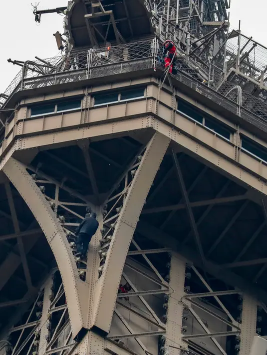 Petugas pemadam kebakaran berusaha mendekati seorang pria yang memanjat Menara Eiffel tanpa peralatan keselamatan di Paris, Senin (20/5/2019). Pasukan pemadam kebakaran harus turun dari lantai tiga dek observasi Menara Eiffel untuk mencapai pria itu. (FRANCOIS GUILLOT / AFP)