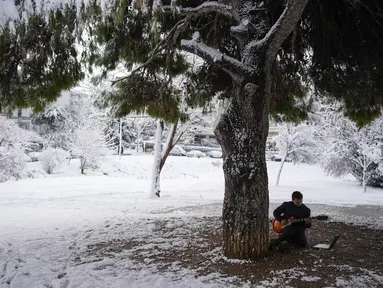 Goulielmos, 24 tahun, bermain gitar di sebuah taman di Vrilisia, pinggiran kota Athena, pada Senin (6/3/2023). Cuaca dingin yang melanda Yunani selatan menyebabkan pemadaman listrik, penutupan jalan raya, dan gangguan layanan. Sekolah-sekolah ditutup di Athena, bersama dengan gedung pengadilan dan beberapa layanan. (AP Photo/Thanassis Stavrakis)