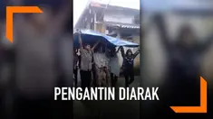Hujan yang turun tak menghalangi pengantin ini untuk menjalani prosesi pernikahan. Keduanya diarak dan dipayungi warga menggunakan terpal plastik sampai ke tenda pelaminan.
