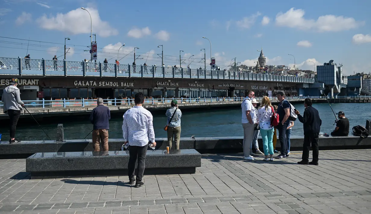 Orang-orang berdiri di dermaga Golden Horn, di depan Jembatan Galata di Istanbul, Turki pada Senin (17/5/2021). Pemerintah Turki mencabut lockdown atau penguncian penuh selama 17 hari untuk mengekang lonjakan infeksi virus corona COVID-19. (OZAN KOSE / AFP)