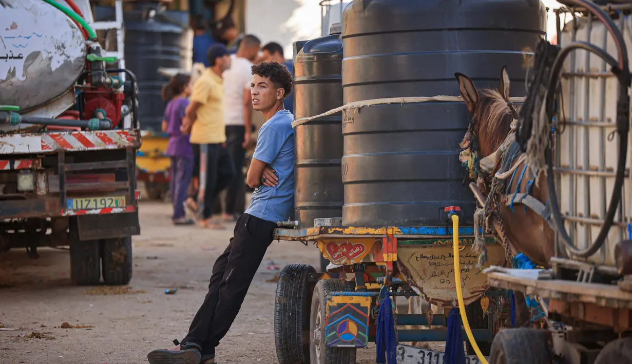 Warga Palestina berkumpul di samping gerobak yang ditarik keledai yang dimuat dengan tangki air untuk dijual. (MAHMUD HAMS/AFP)