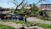 Seorang pria berjalan melewati pohon besar yang menghalangi jalan setelah badai dahsyat melanda St. Louis, Missouri, AS [Jeff Roberson/AP]