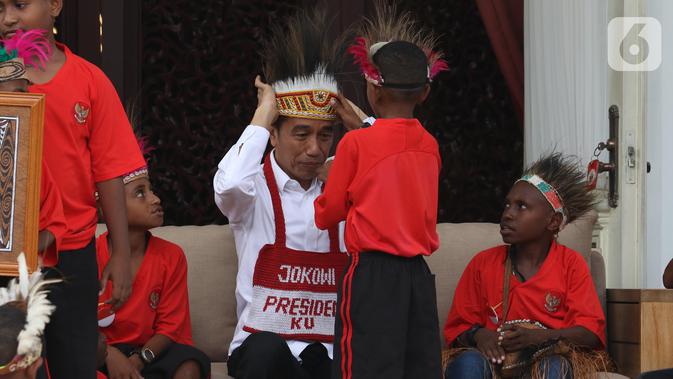 Presiden Joko Widodo atau Jokowi memasang topi rumbai saat menerima perwakilan anak-anak sekolah dasar dari Papua di Istana Merdeka, Jakarta, Jumat (11/10/2019). Jokowi mengaku sudah berjanji untuk mengundang mereka ke istana saat mengunjungi Jayapura dan Asmat. (Liputan6.com/Angga Yuniar)