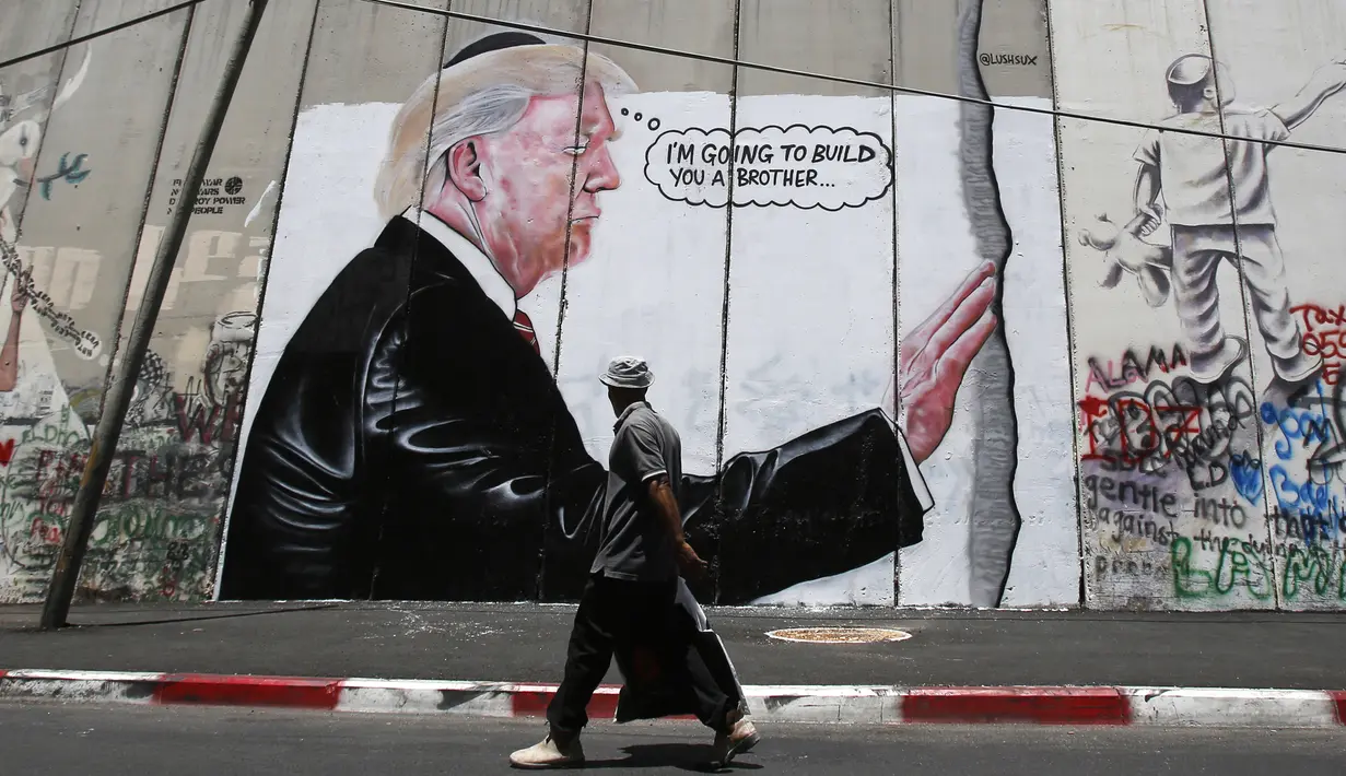 Seorang pria Palestina berjalan didepan grafiti yang menggambarkan Presiden AS Donald Trump di tembok pemisah Israel - Palestina di kota Bethlehem (4/8). Tembok di Tepi Barat ini membentang sepanjang 700 kilometer. (AFP Photo/Musa Al Shaer)