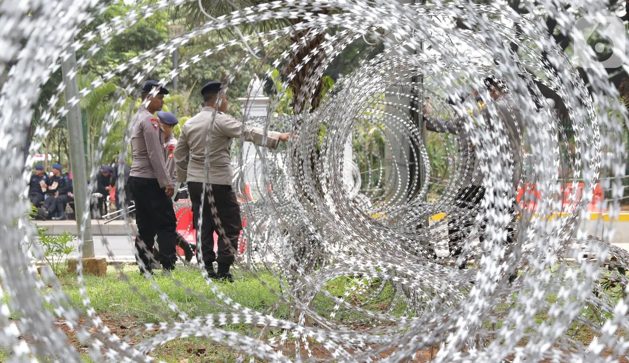 Personel Kepolisian berjaga dibalik barikade kawat berduri yang menutup ruas Jalan Medan Merdeka Barat, Jakarta, Senin (28/10/2019). Penutupan ini antisipasi aksi unjuk rasa mahasiswa mendesak Presiden Jokowi segera mengeluarkan Perppu KPK. (Liputan6.com/Helmi Fithriansyah)