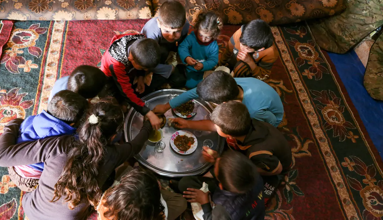 Beberapa cucu dari Abderrazaq Khatoun berbagi makanan di dalam tenda di desa Harbanoush, Suriah, 11 Maret 2021. Mengungsi dari rumah asalnya di provinsi Hama, Khatoun dan 30 anggota keluarga yang masih hidup mendirikan empat tenda di sebidang tanah yang dikelilingi pohon zaitun (Ahmad al-ATRASH/AFP)