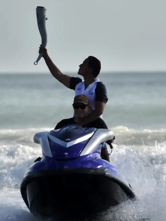 Aktor Hamish Daud membawa obor Asian Games 2018 saat dibawa berselancar ke tengah laut di Pantai Kuta, Bali, Senin (23/7). Api obor Asian Games sempat padam saat Hamish Daud membawa obor sambil berselancar di Pantai Kuta. (AFP/SONNY TUMBELAKA)