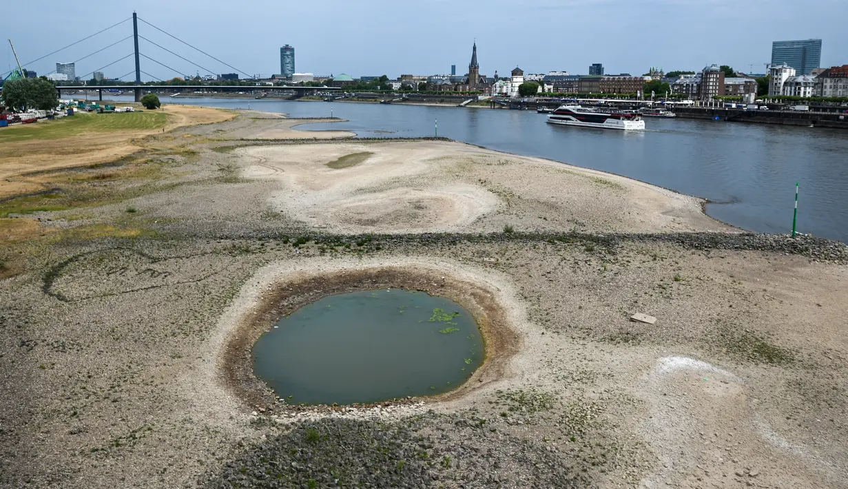 <p>Sebuah kapal pedalaman berlayar di Rhine saat dasar sungai yang mengering sebagian terlihat di latar depan di Duesseldorf, Jerman barat (25/7/2022). Sungai Rhine adalah salah satu rute pelayaran terpenting di benua Eropa dan tentu saja merupakan jalur air terpenting Jerman. (AFP/Photo/Ina Fassbender)</p>