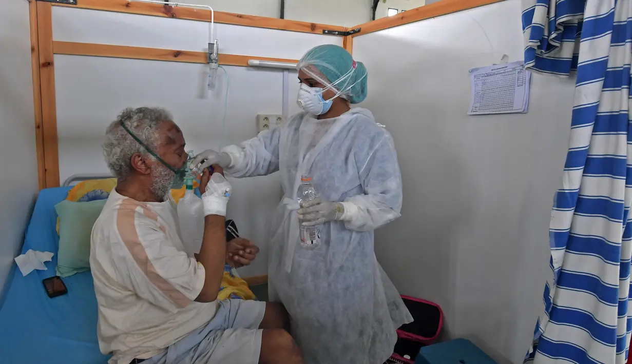 Seorang petugas medis Tunisia merawat pasien di gym yang diubah untuk menangani lonjakan infeksi COVID-19 di pusat kota Kairouan pada 4 Juli 2021. Tunisia tengah berjuang menghadapi tsunami COVID-19 sementara jumlah orang yang meninggal akibat virus corona terus melonjak tinggi. (FETHI BELAID/AFP)