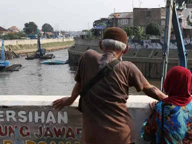 Warga menyaksikan proses pengerukan endapan tanah di aliran Sungai Ciliwung, Jakarta, Selasa (28/7/2020). Pengerukan endapan ini untuk memperlancar aliran air Sungai Ciliwung serta upaya pencegahan banjir saat musim hujan. (Liputan6.com/Helmi Fithriansyah)