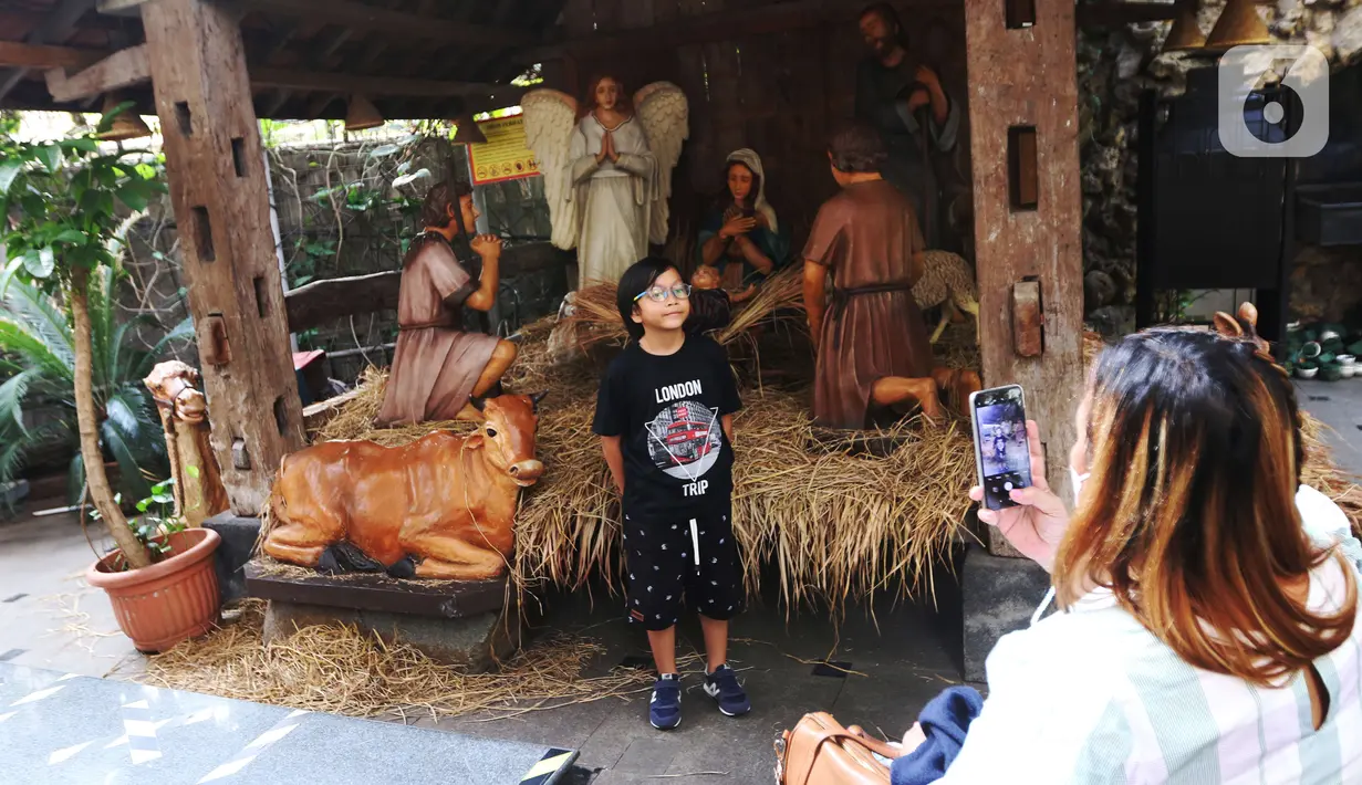 Seorang anak berfoto dengan diorama bernuansa Natal di lingkungan Gereja Katedral, Jakarta, Rabu (22/12/2021). Jemaat yang akan beribadah di Gereja Katedral Jakarta nantinya akan dibatasi untuk mencegah penularan COVID-19. (Liputan6.com/Angga Yuniar)