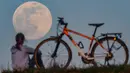 Pengendara sepeda berhenti untuk menyaksikan supermoon di Sieversdorf, Jerman, Selasa (7/4/2020). Fenomena dimana bulan berada pada titik terdekat dengan bumi ini merupakan penampakan supermoon terbesar di tahun 2020. (Patrick Pleul /dpa/AFP)