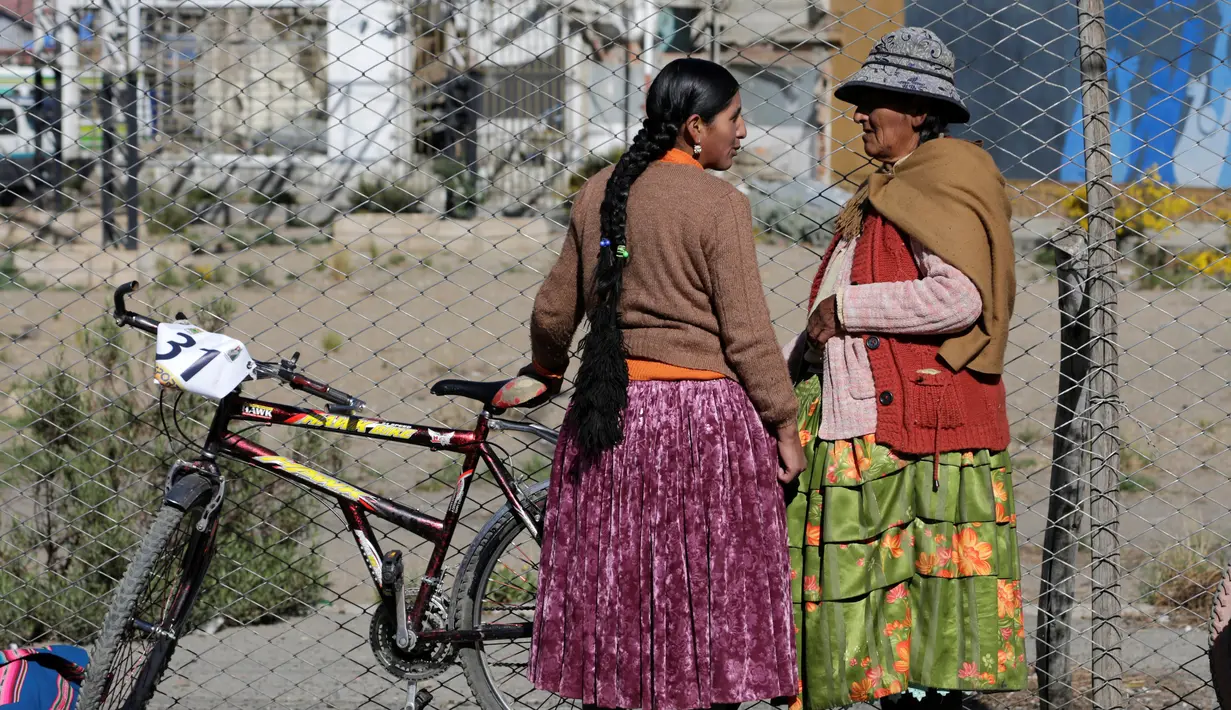 Seorang peserta berbincang dengan ibunya sebelum balapan sepeda Cholita dimulai di El Alto, La Paz, Bolivia (29/10). Peserta yang ikut wajib menggunakan rok tradisional setempat dan mengikat kepang rambut mereka. (Reuters/David Mercado)