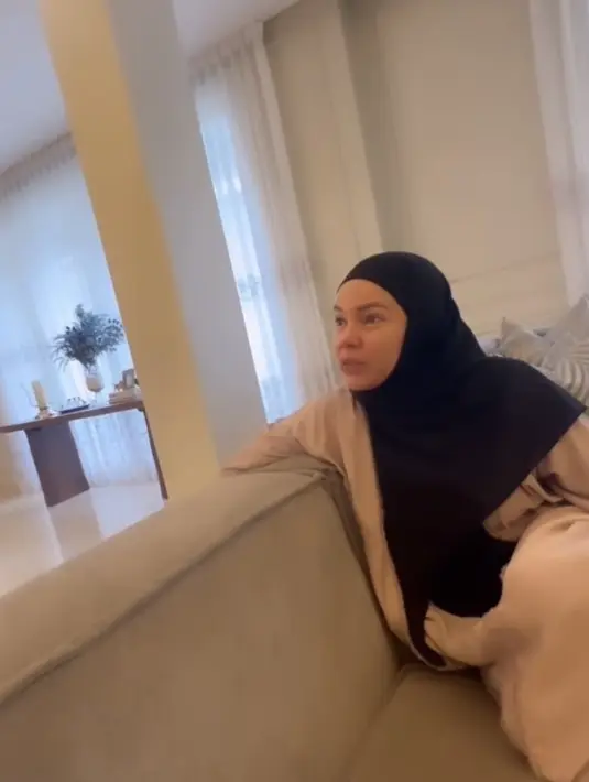 Saat berkunjung ke rumah Olla, Dewi pun tampak santai duduk di sofa panjang. Terlihat ia mengenakan outer panjang warna beige dipadukan dress panjang loose hitam, senada dengan kerudung panjangnya. [@ollaramlan]