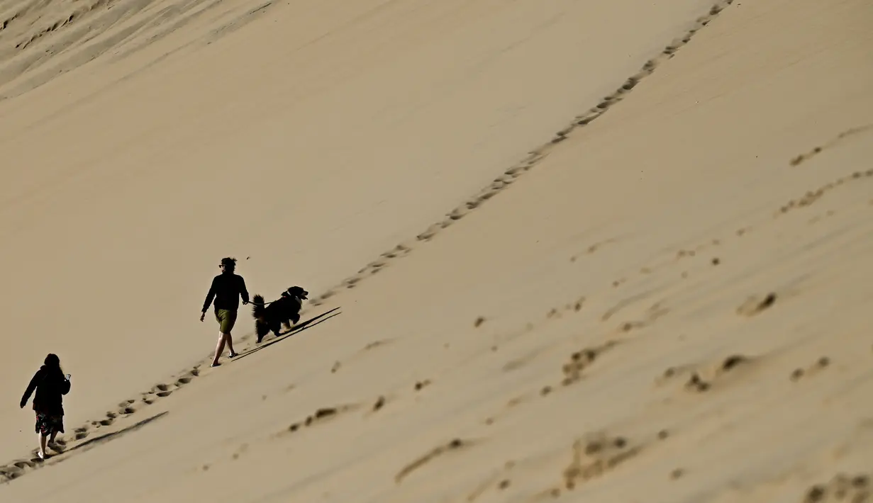 Orang-orang menikmati hari yang cerah di atas gundukan pasir tertinggi di Eropa yang disebut "Dune du Pilat" di La Teste-de-Buch, dekat Teluk Arcachon di Prancis pada 3 April 2021. Karena keindahan dan keeksotisannya, bukit pasir ini banyak didatangi wistawan setiap tahunnya. (Philippe LOPEZ / AFP)