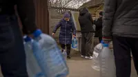 Penduduk setempat mengisi botol mereka dengan air yang mereka ambil dari air mancur umum di Bucha, di pinggiran Kiev, Ukraina pada Senin (18/4/2022). Warga Bucha masih tanpa listrik, air dan gas setelah lebih dari 43 hari sejak invasi Rusia. (AP Photo/Emilio Morenatti)