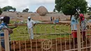 Buruh bekerja di taman dekat batu 'Krishna's Butter Ball' yang terkenal di Mahabalipuram, India, Kamis (3/10/2019). Posisi batu yang aneh itu lantas jadi populer di kalangan wisatawan yang memakainya untuk latar belakang pose lucu saat berfoto. (ARUN SANKAR / AFP)